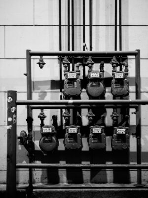 Black and white of aged gas meters attached to thin iron pipes near wall