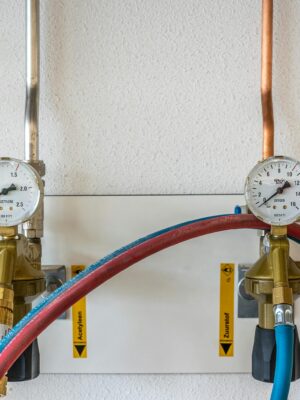 Close-up of industrial gas pressure gauges connected with hoses against a white wall.